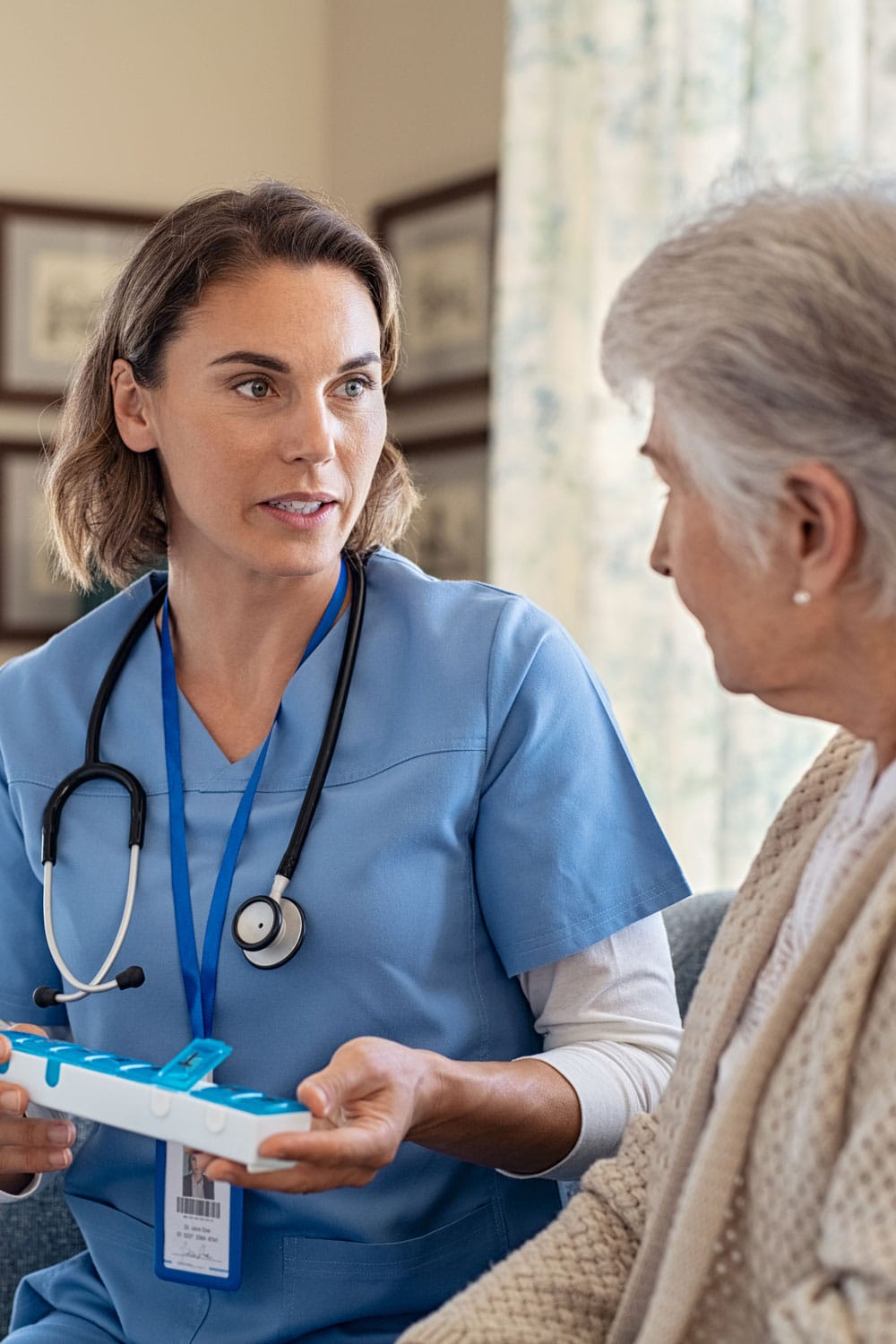 A nurse holding a pill box talking with an elderly woman